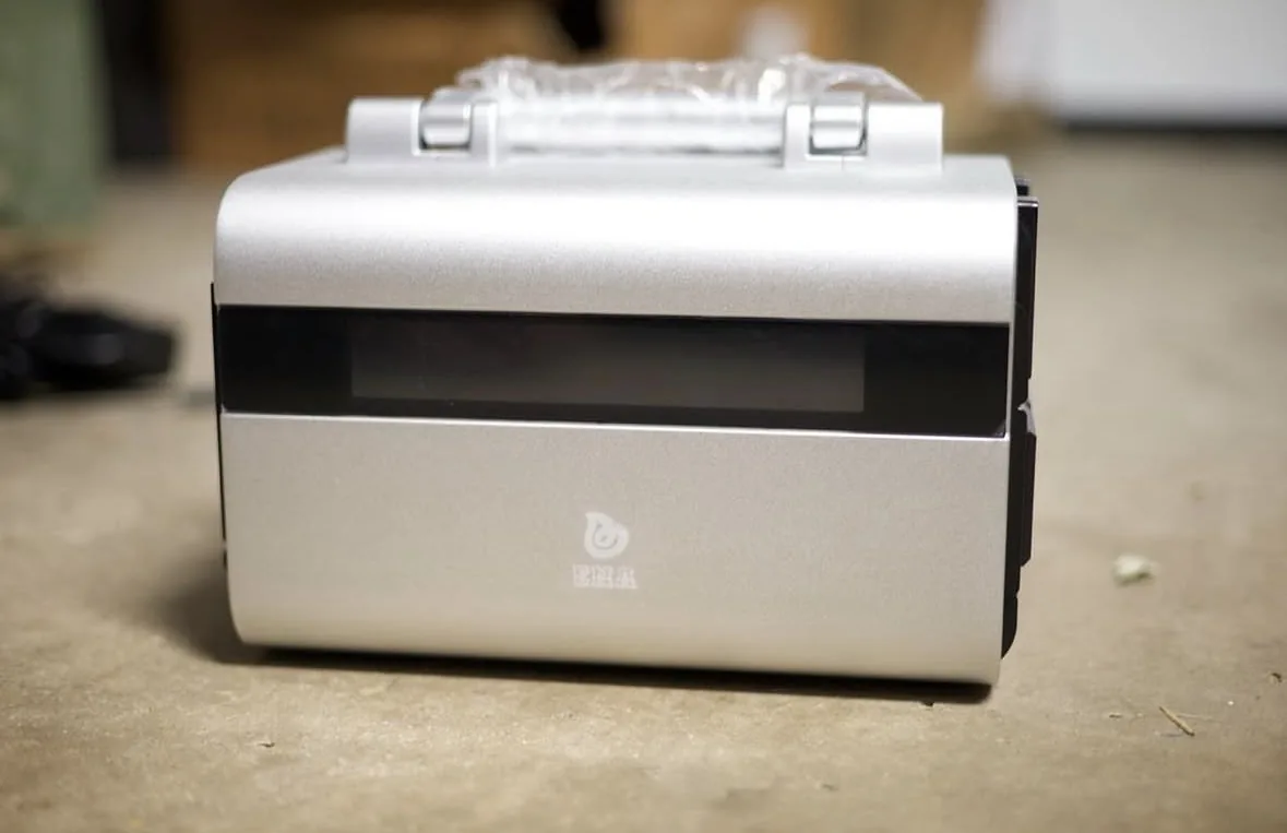 An ENA POPS portable power station on a workshop floor, showing its wide front display panel, carry handles and the ENA logo