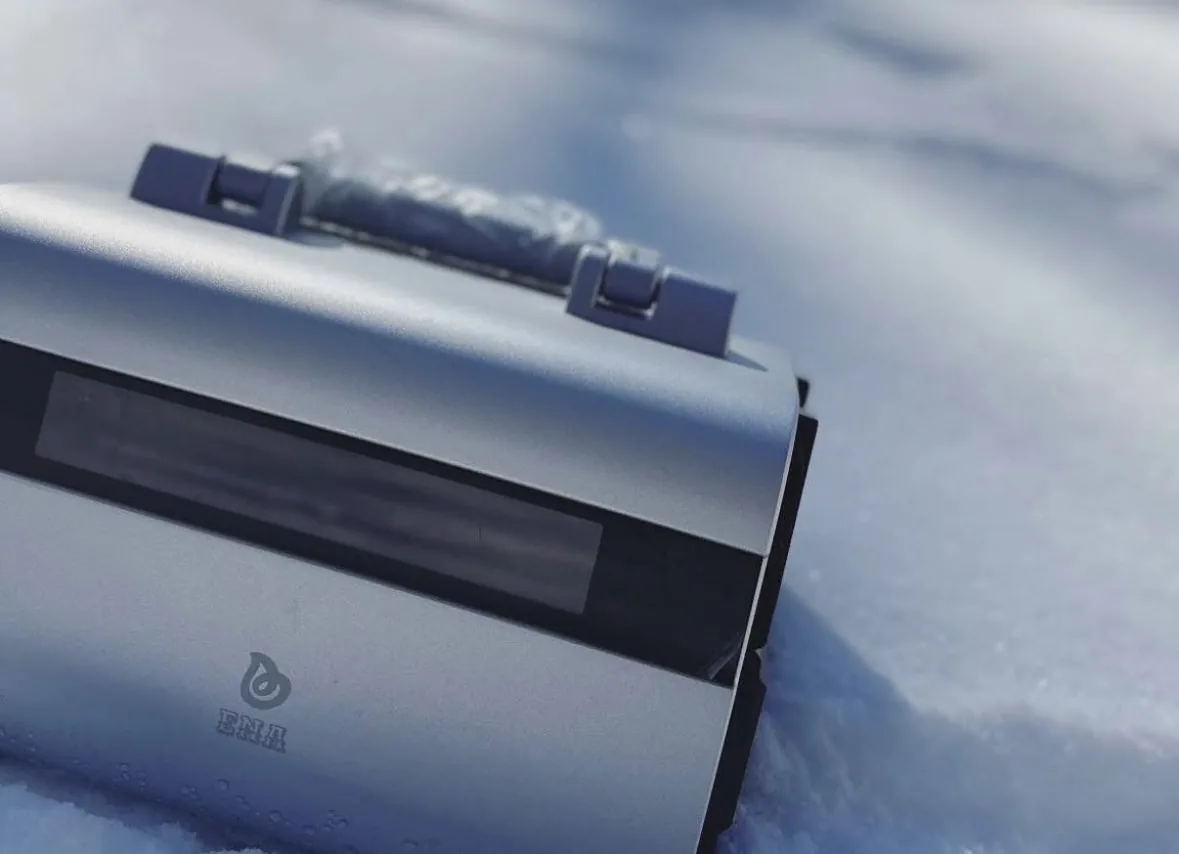 An ENA POPS portable power station standing in deep snow in bright sunlight, its display visible